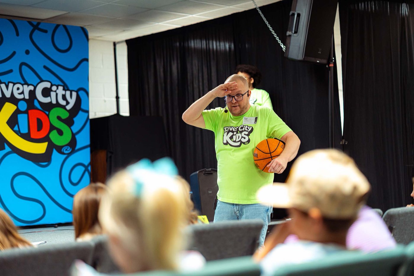 A kids leader holding a basketball during a game, children watching from their seats